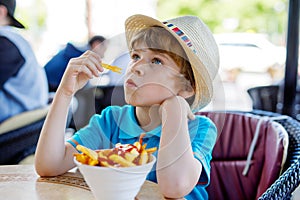 Cute healthy preschool kid boy eats french fries potatoes with ketchup