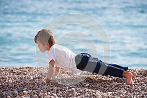 Cute healthy strong kid making pushups with effort on sea coast in autumn