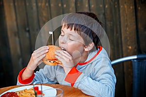 Cute healthy teenager boy eats hamburger