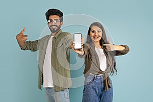 Cute hindu couple showing cell phone with white screen, mockup
