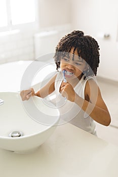 Cute hispanic boy with curly black hair brushing teeth in bathroom at home