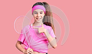 Cute hispanic child girl holding badminton racket smiling happy pointing with hand and finger