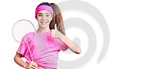 Cute hispanic child girl holding badminton racket smiling happy and positive, thumb up doing excellent and approval sign