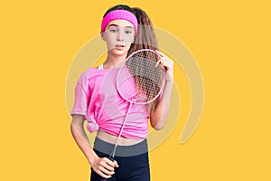 Cute hispanic child girl holding badminton racket thinking attitude and sober expression looking self confident