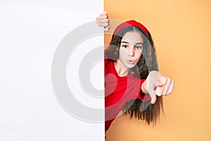 Cute hispanic child girl holding blank empty banner pointing with finger to the camera and to you, confident gesture looking