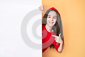 Cute hispanic child girl holding blank empty banner pointing finger to one self smiling happy and proud