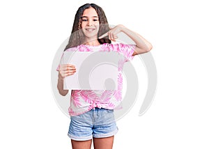 Cute hispanic child girl holding blank empty banner pointing finger to one self smiling happy and proud