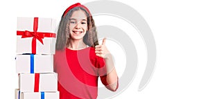 Cute hispanic child girl holding gift smiling happy and positive, thumb up doing excellent and approval sign