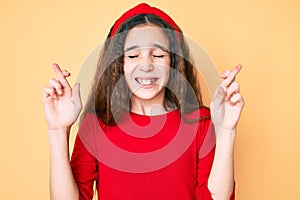 Cute hispanic child girl wearing casual clothes and diadem gesturing finger crossed smiling with hope and eyes closed