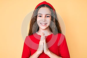 Cute hispanic child girl wearing casual clothes and diadem praying with hands together asking for forgiveness smiling confident