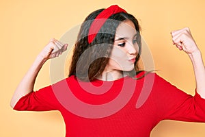 Cute hispanic child girl wearing casual clothes and diadem showing arms muscles smiling proud