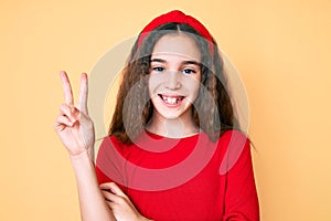 Cute hispanic child girl wearing casual clothes and diadem smiling with happy face winking at the camera doing victory sign