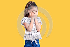 Cute hispanic child girl wearing casual clothes with sad expression covering face with hands while crying