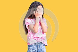 Cute hispanic child girl wearing casual clothes with sad expression covering face with hands while crying