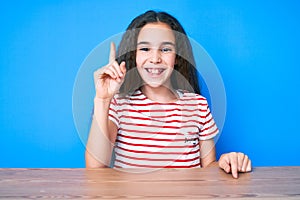 Cute hispanic child girl wearing casual clothes sitting on the table pointing finger up with successful idea