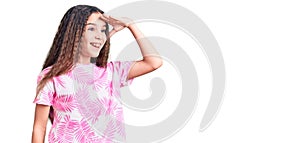 Cute hispanic child girl wearing casual clothes very happy and smiling looking far away with hand over head