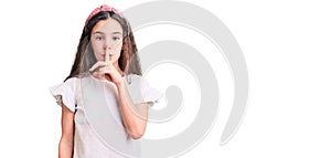 Cute hispanic child girl wearing casual white tshirt asking to be quiet with finger on lips