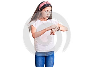 Cute hispanic child girl wearing casual white tshirt checking the time on wrist watch, relaxed and confident