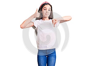 Cute hispanic child girl wearing casual white tshirt doing thumbs up and down, disagreement and agreement expression