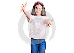 Cute hispanic child girl wearing casual white tshirt looking at the camera smiling with open arms for hug