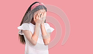 Cute hispanic child girl wearing casual white tshirt with sad expression covering face with hands while crying