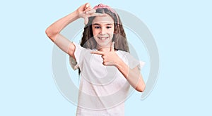 Cute hispanic child girl wearing casual white tshirt smiling making frame with hands and fingers with happy face
