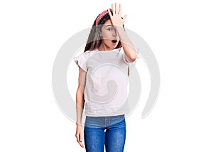 Cute hispanic child girl wearing casual white tshirt surprised with hand on head for mistake, remember error