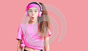 Cute hispanic child girl wearing gym clothes and using headphones afraid and shocked with surprise expression, fear and excited