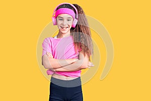 Cute hispanic child girl wearing gym clothes and using headphones happy face smiling with crossed arms looking at the camera