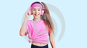 Cute hispanic child girl wearing gym clothes and using headphones pointing finger up with successful idea