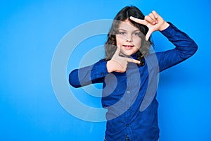 Cute hispanic child with long hair wearing casual clothes smiling making frame with hands and fingers with happy face