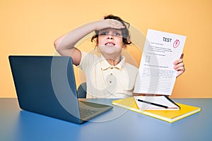 Cute hispanic child showing failed exam sitting on the desk stressed and frustrated with hand on head, surprised and angry face