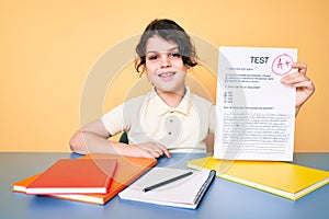 Cute hispanic child showing a passed exam sitting on the desk looking positive and happy standing and smiling with a confident