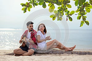 Cute hispanic couple playing guitar serenading on beach in love and embrace, happy and relax outdoor on the sand.