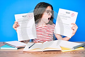 Cute hispanic girl showing failed and passe exam sitting on the table angry and mad screaming frustrated and furious, shouting