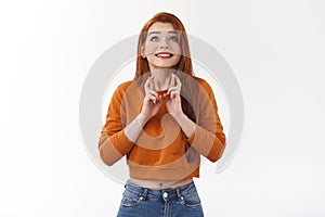 Cute hopeful redhead girl look up sky implore god wish come true smiling delighted faithfully praying cross fingers good photo