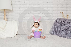 Cute Indian baby girl with pink bunny ears and basket of colorful eggs celebrating Easter holiday