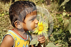 Cute Indian child with sunflower on nature background in summer garden.