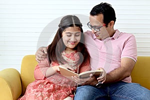 Cute Indian school student girl wears traditional dress sitting with father in living room and doing homework, dad teaching