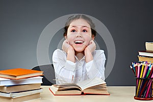 Cute industrious child is sitting at a desk indoors. Kid is learning in class on background of blackboard.