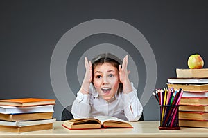 Cute industrious child is sitting at a desk indoors. Kid is learning in class on background of blackboard.