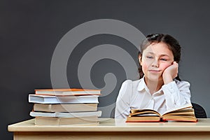 Cute industrious child is sitting at a desk indoors. Kid is learning in class on background of blackboard.