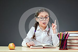Cute industrious child is sitting at a desk indoors. Kid is learning in class on background of blackboard.