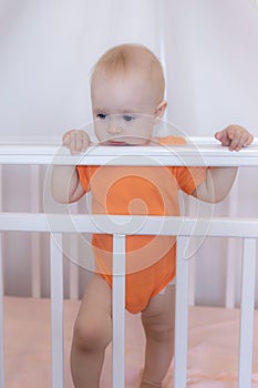 A cute infant baby standing in a crib in a pink bedroom scene