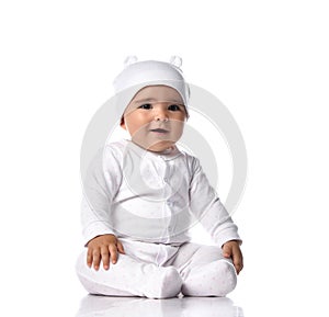Cute infant baby toddler in white jumpsuit overall and funny hat with ears sits on the floor with opened mouth and sings