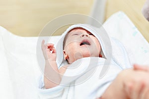 Cute infant baby in white towel crying after first bathing at bathroom. Newborn children healthcare and hygiene