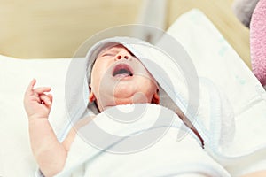 Cute infant baby in white towel crying after first bathing at bathroom. Newborn children healthcare and hygiene