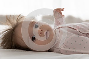 Cute infant in bodysuit lying on bed looking at camera