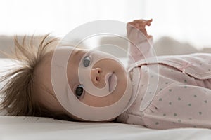 Cute infant in bodysuit lying on bed looking at camera photo
