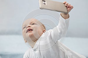 Cute infant boy makes selfie with a cell phone. Adorable smiling toddler kid taking a selfie photo with smartphone.